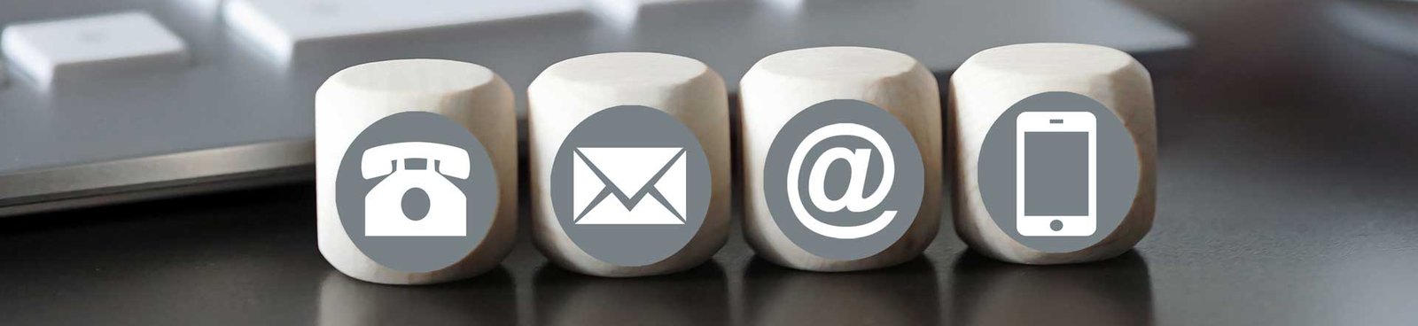 Four wooden blocks with gray contact icons: a landline phone, an envelope for email, an @ symbol, and a smartphone.
