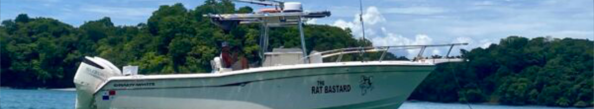 Powerboat named The Rat Bastard cruising on blue water with a forested shoreline in the background.