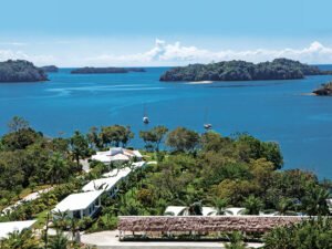 - Panama Sport Fishing Charters Aerial view of a tropical island resort with white buildings among palm trees along the shoreline, blue water, and two sailboats in the bay.