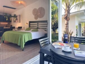 - Panama Sport Fishing Charters Hotel room seen through glass doors with a green-bedspread and a patio table set for breakfast outside, including juice, coffee, and watermelon slices.