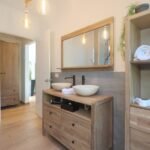 bdm11 - Panama Sport Fishing Charters Wooden bathroom vanity with two vessel sinks and a large framed mirror; warm Edison bulbs and open shelving with rolled towels create a rustic-modern look.