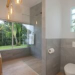 bdm13 - Panama Sport Fishing Charters Bright modern bathroom with a glass-enclosed shower, wooden vanity with vessel sinks, and a view of a green garden through a large window.