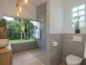 - Panama Sport Fishing Charters Bright modern bathroom with a glass-enclosed shower, wooden vanity with vessel sinks, and a view of a green garden through a large window.