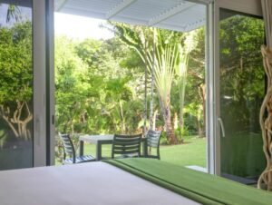 - Panama Sport Fishing Charters View from inside looking out to a sunny backyard with a patio table and four chairs among tropical plants.