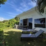 bdm17 - Panama Sport Fishing Charters White vacation villa with glass doors, two lounge chairs on a grassy lawn, and a lake view with tropical plants nearby?