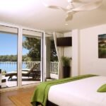 bdm20 - Panama Sport Fishing Charters Bright hotel bedroom with a large sliding-glass door opening to a balcony view of blue water and trees outside.