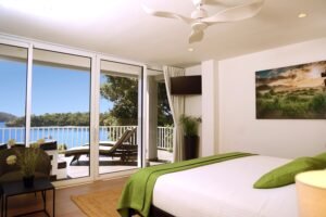- Panama Sport Fishing Charters Bright hotel bedroom with a large sliding-glass door opening to a balcony view of blue water and trees outside.