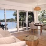 bdm21 - Panama Sport Fishing Charters Bright open-plan living and dining area with large sliding glass doors to a balcony overlooking water; beige sofa, round glass coffee table, and a wooden dining table with four chairs.