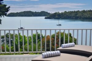 - Panama Sport Fishing Charters Balcony with two lounge chairs and rolled white towels overlooking a calm bay with sailboats and green trees.