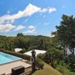 bdm23 - Panama Sport Fishing Charters Swimming pool in a villa garden with lush tropical plants and a blue bay in the background, a small sailboat on the water.