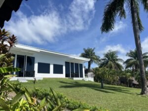 - Panama Sport Fishing Charters White, single-story house with a covered patio on a green lawn, surrounded by palm trees under a bright blue sky.
