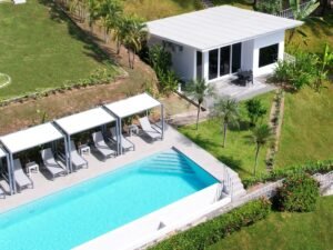 - Panama Sport Fishing Charters Aerial view of a rectangular blue pool with white edge, surrounded by four cabanas with lounge chairs and small tables, on a sunny resort lawn.