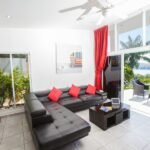 bdm27 - Panama Sport Fishing Charters Bright modern living room with a black sectional sofa and red cushions, facing a coffee table, opening to a sunny patio by the water.