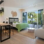 bdm5 - Panama Sport Fishing Charters Bright, open-plan studio with a bed in green bedding, a seating area, and a balcony view of palm trees outside.