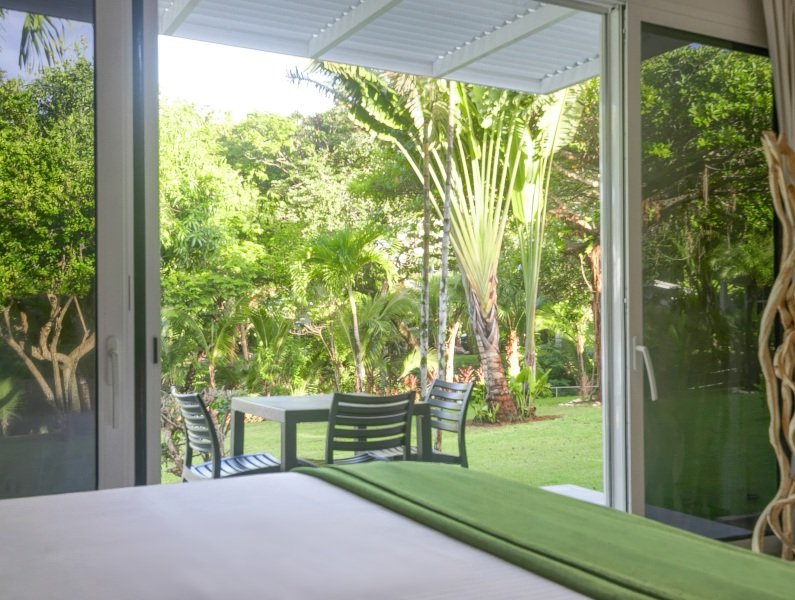 Open sliding doors reveal a sunny backyard with a white table and black chairs on the lawn.