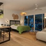 bdm8 - Panama Sport Fishing Charters Studio hotel room with a bed, green bedspread, dining table, and a sofa near large windows opening to a balcony at dusk.