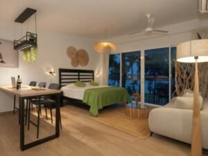 - Panama Sport Fishing Charters Studio hotel room with a bed, green bedspread, dining table, and a sofa near large windows opening to a balcony at dusk.