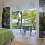 bdm9 - Panama Sport Fishing Charters Bedroom with a green bedspread opens to a patio with a table and chairs, overlooking a lawn and lake.
