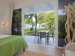 - Panama Sport Fishing Charters Bedroom with a green bedspread opens to a patio with a table and chairs, overlooking a lawn and lake.