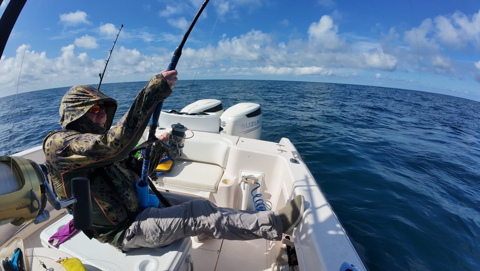 default - Panama Sport Fishing Charters Fisherman in a camo hooded jacket fishing from a small white boat on a blue ocean under a bright sky.