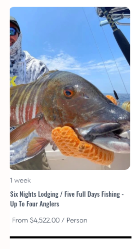 Fisherman on a boat wearing a hoodie and sunglasses, holding a large striped fish with orange gloves against a blue sky.