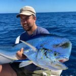 Man on a boat holding a large blue marlin, with a blue ocean in the background.