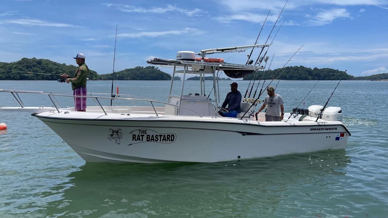 White sport fishing boat named The Rat Bastard with four men fishing in calm blue-green water near tree-covered islands in the background.