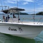 White fishing boat named 'The Rat Bastard' with a cartoon rat logo on calm blue water.